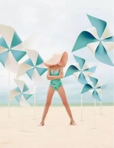 Editorial vintage: modelo con pamela y traje de baño verde entre molinos de viento de papel en la playa
