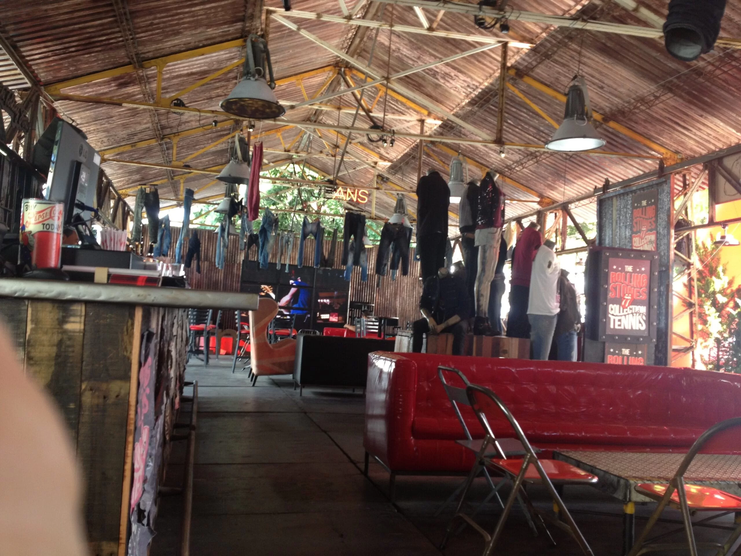 Interior del stand de Tennis con techo de zinc, ropa colgada y sofás rojos en Colombiamoda 2013