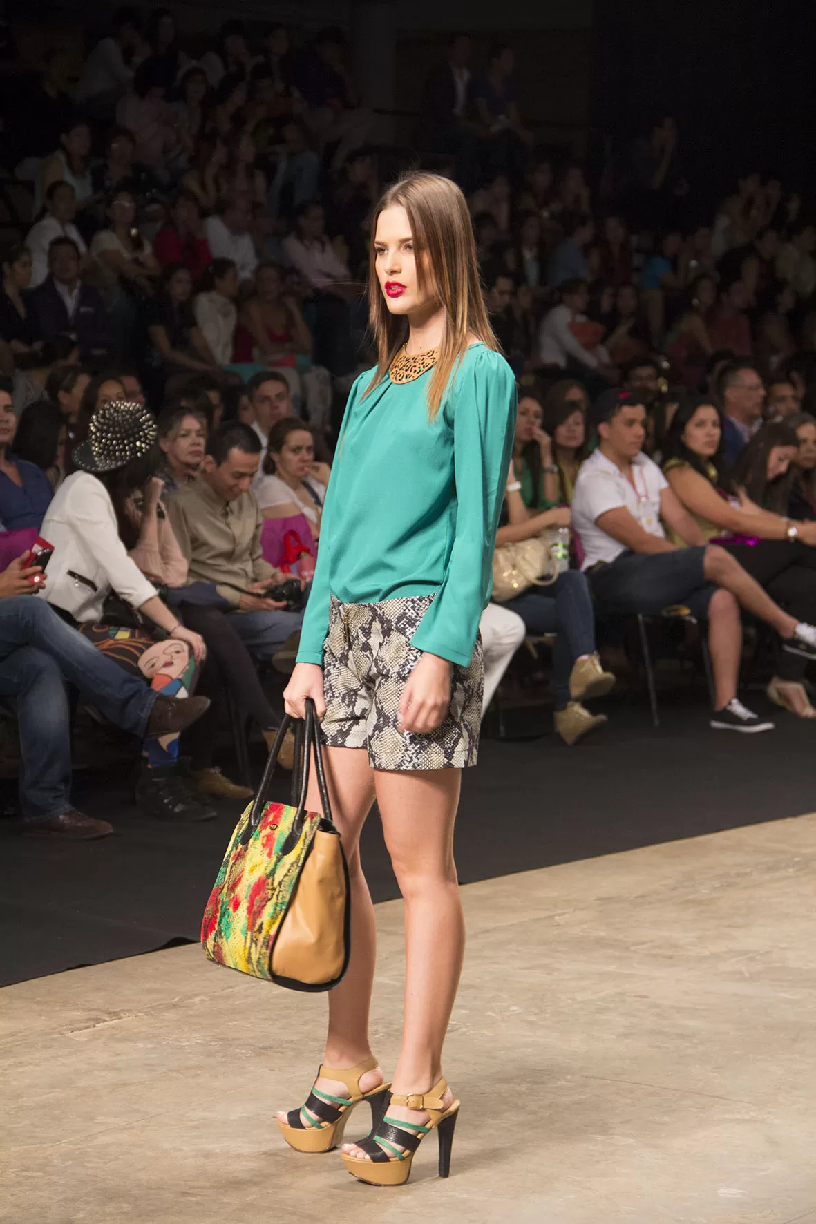 Modelo con blusa verde, short estampado y bolso floral de SIUK ante el público del SFW 2013