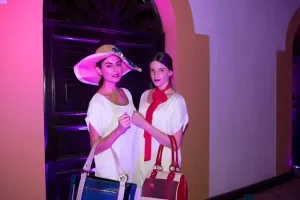 Dos modelos con sombrero, blusa blanca y bolsos posan bajo luces rosadas en el lanzamiento del SFW 2013