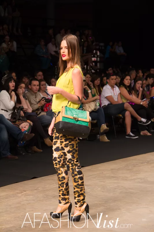 Modelo con blusa amarilla, pantalón de animal print y bolso verde de SIUK en la pasarela del SFW 2013