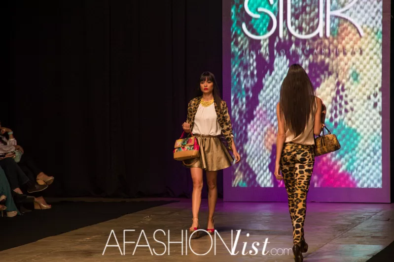 Modelos con blazer y pantalón de animal print y bolsos de SIUK frente a la pantalla de la marca en el SFW 2013