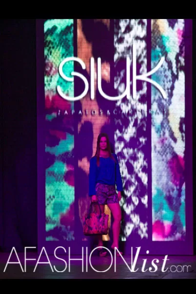 Pantalla con el logo de SIUK y una modelo con blusa azul en la pasarela del SFW 2013