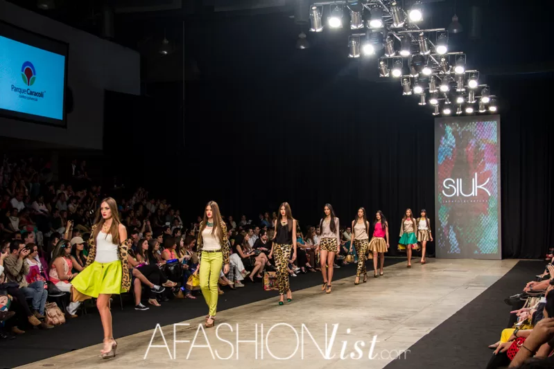 Modelos de SIUK desfilan en fila con bolsos de colores hacia la pantalla de la marca en el SFW 2013