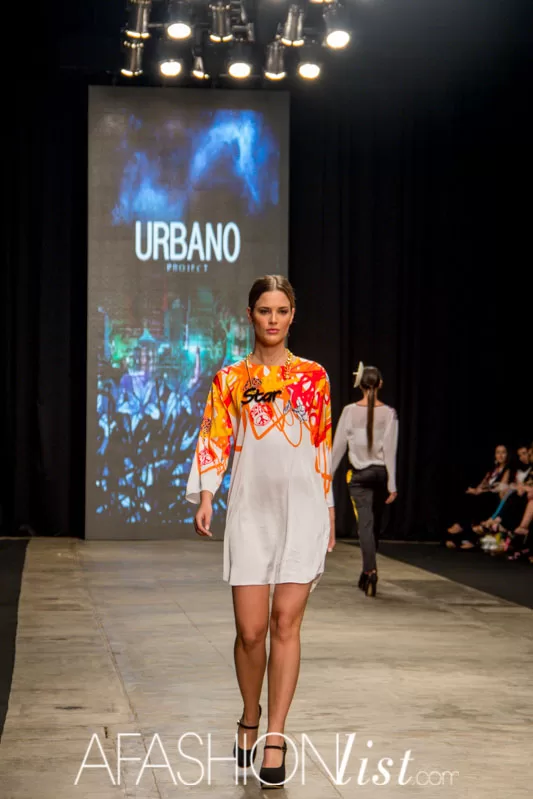 Modelo con vestido blanco con estampado de llamas naranja de Urbano Project frente a la pantalla de la marca, SFW 2013