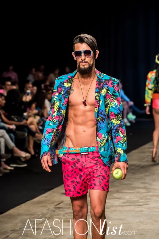 Modelo masculino con blazer estampado tropical y pantaloneta fucsia de Lolos con una manzana verde en el SFW 2013