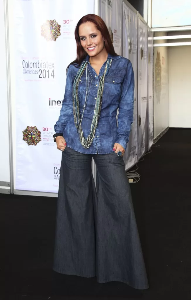 Mujer con camisa de jean, collares y pantalón de jean acampanado frente al backing de Colombiatex 2014