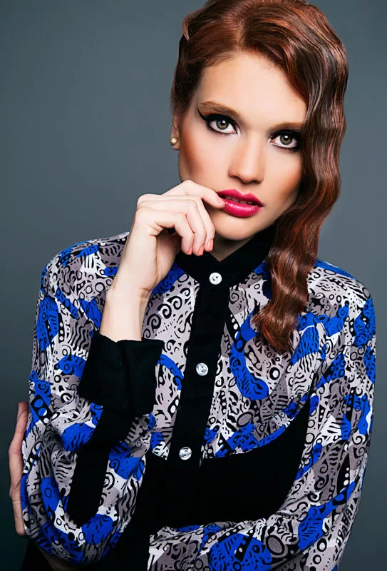 Editorial: modelo pelirroja con blusa estampada azul y negra y labios fucsia sobre fondo gris