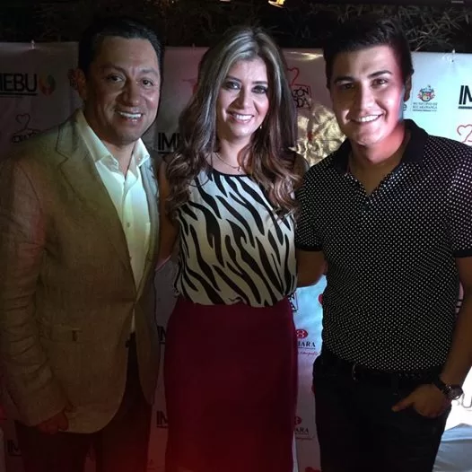 Tres invitados con blusa de cebra y traje beige posan frente al backing de Corazón de la Moda