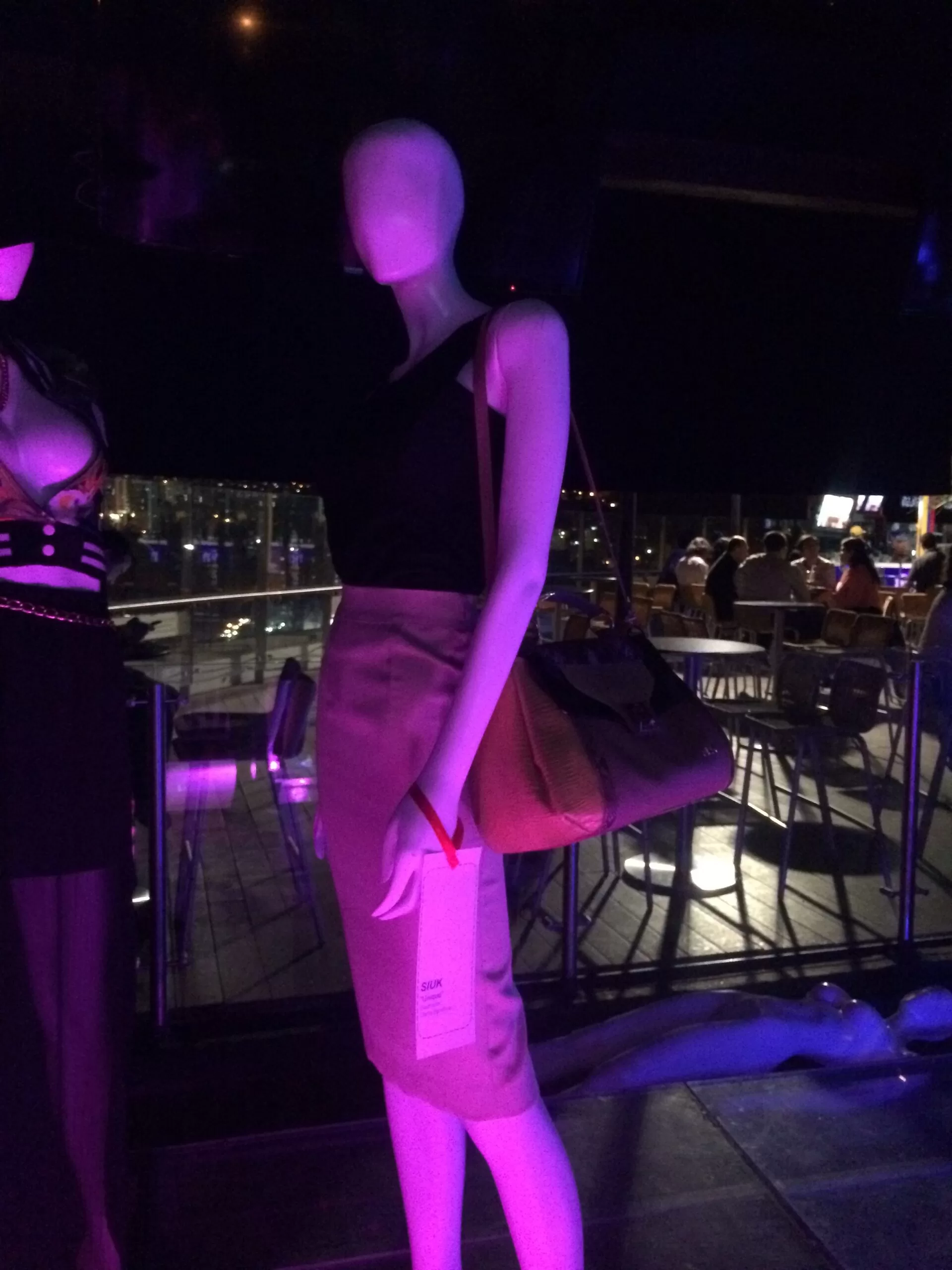 Maniquí con vestido negro y bolso camel bajo luces moradas en el lanzamiento