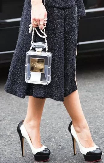 Bolso Chanel transparente de perfume con falda negra y tacones bicolor, street style
